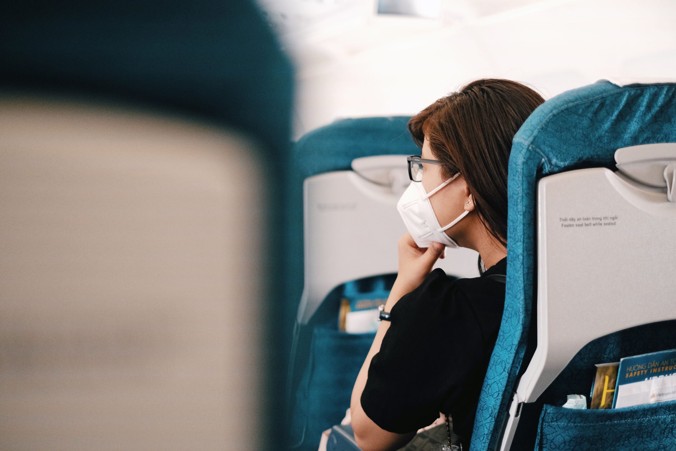 A woman sits on an airplane, wearing a face mask during the flight, representing the new normal of air travel.