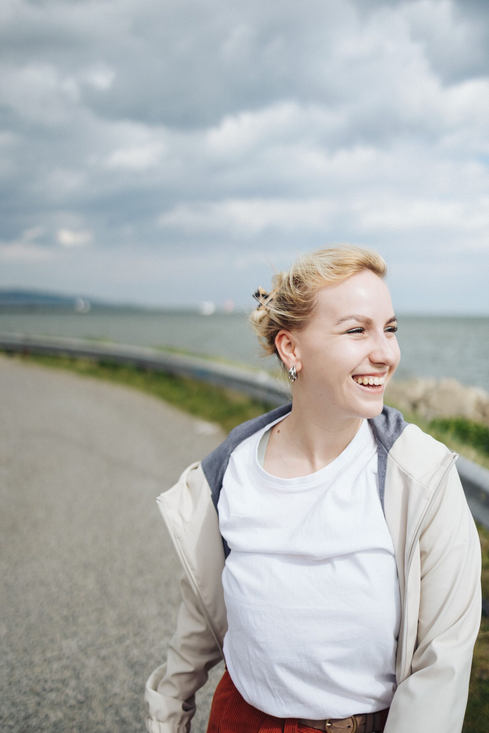 Cheerful woman standing by a coastal road, smiling in the ocean breeze. Perfect for lifestyle and travel themes.
