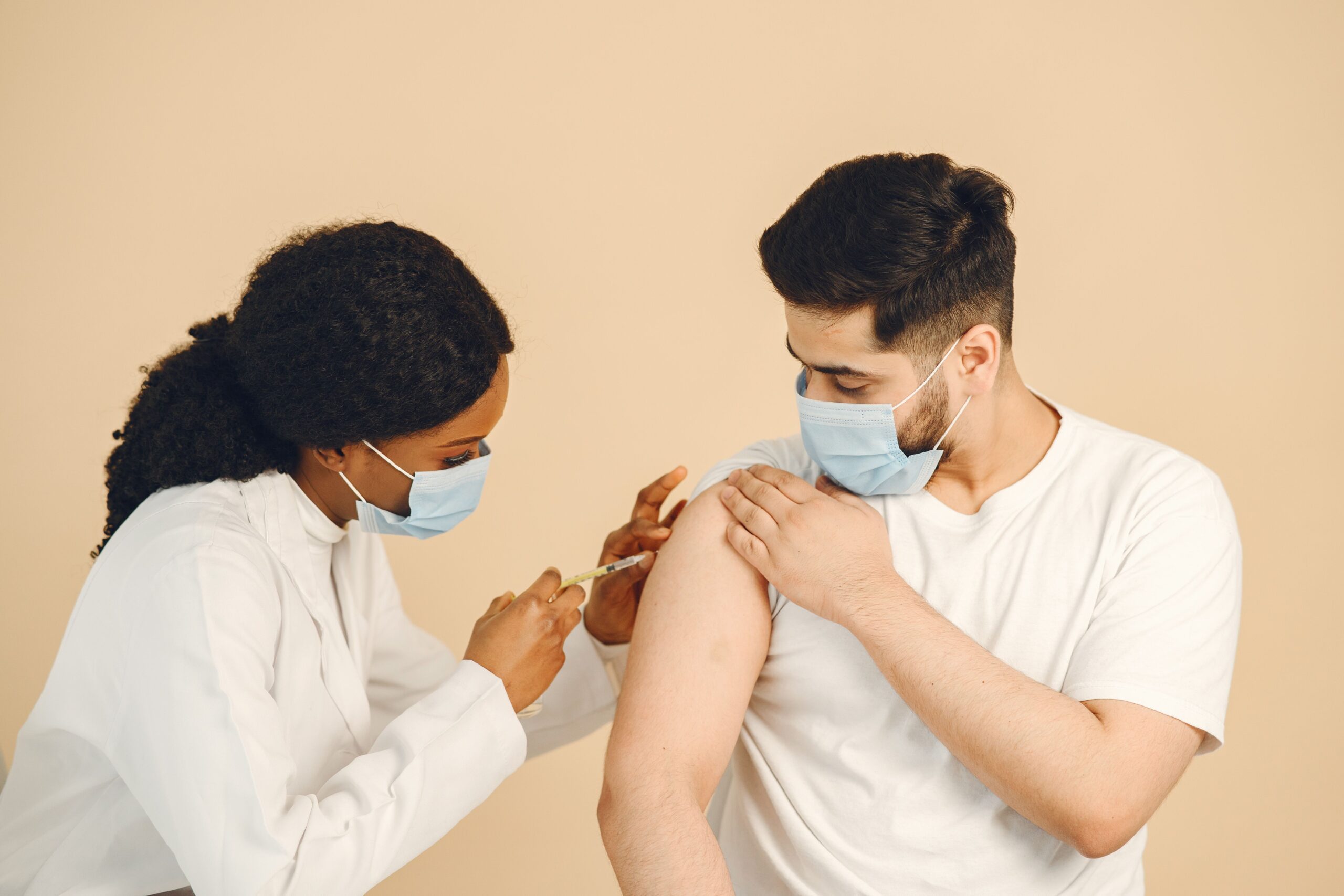 Healthcare worker in mask giving vaccination to a patient in clinical setting.